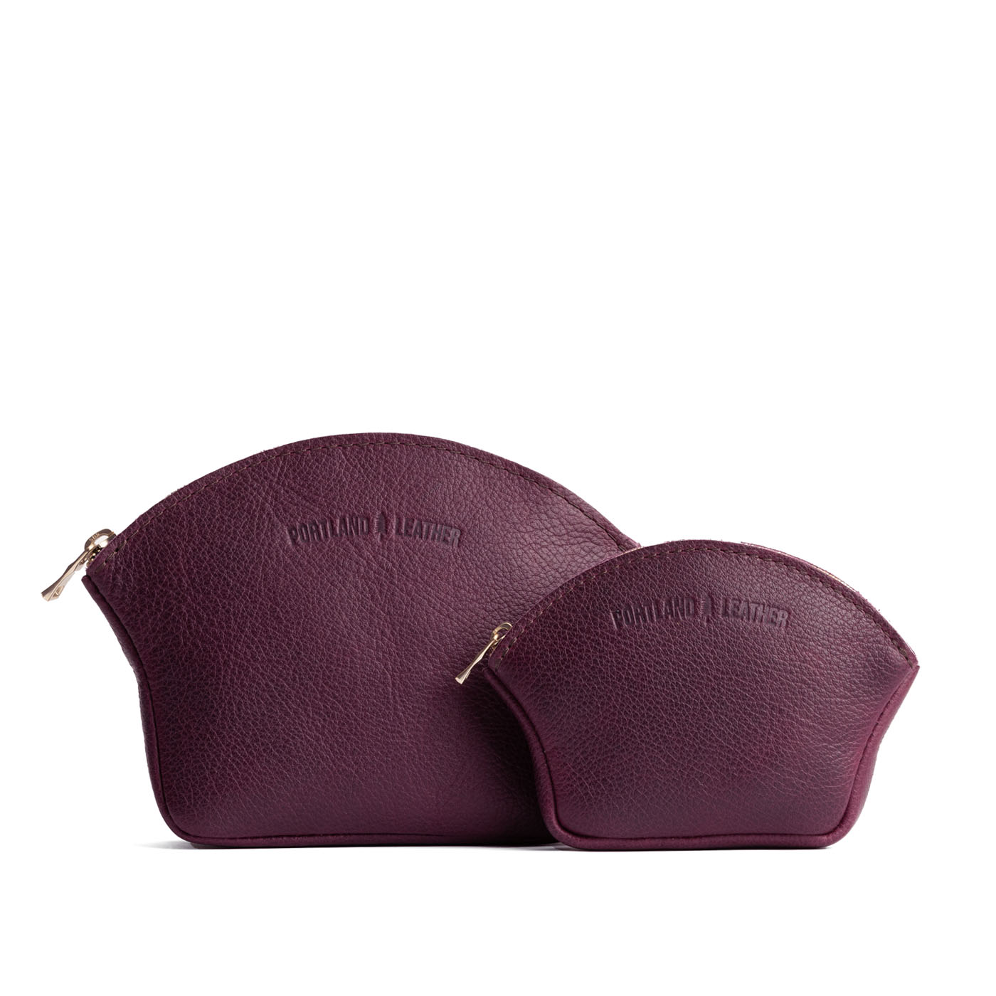 Plum | Comparison shot of small and large seashell shaped leather makeup bags with curved top zipper and flat bottom