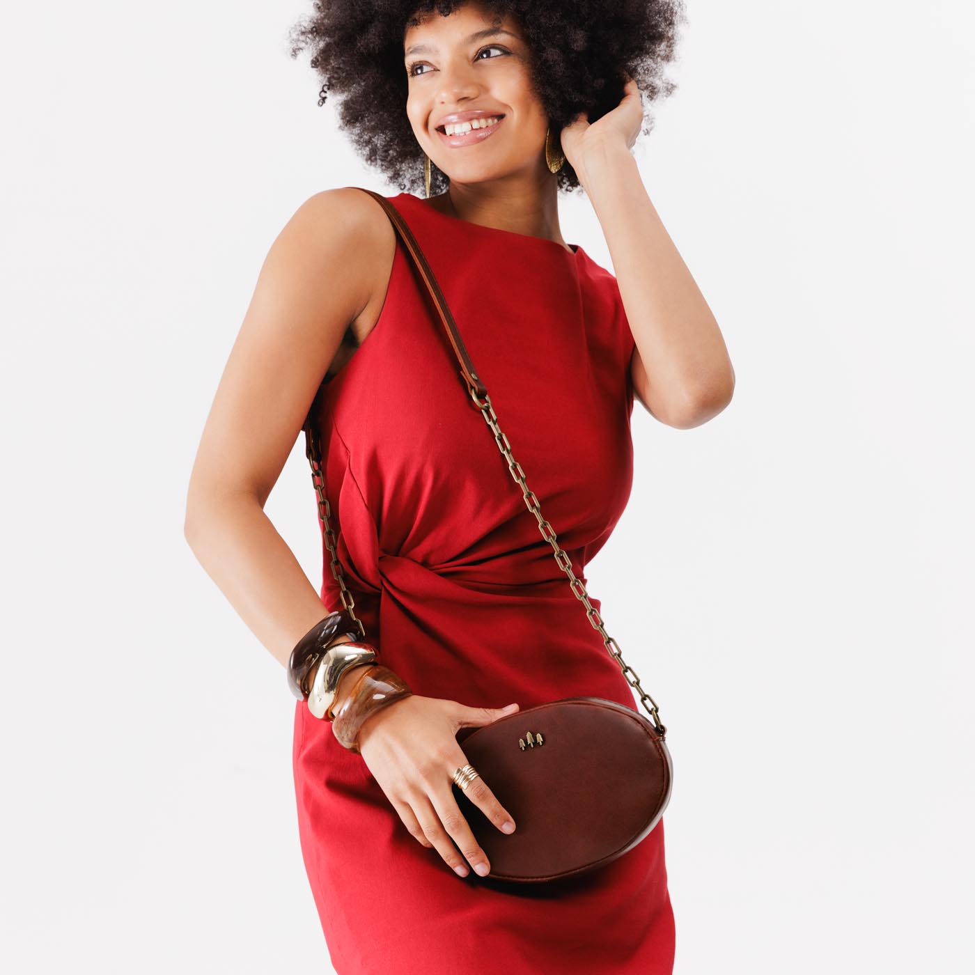 Cognac | Model wearing oval leather purse with metal crossbody chain strap and adjustable leather shoulder guard