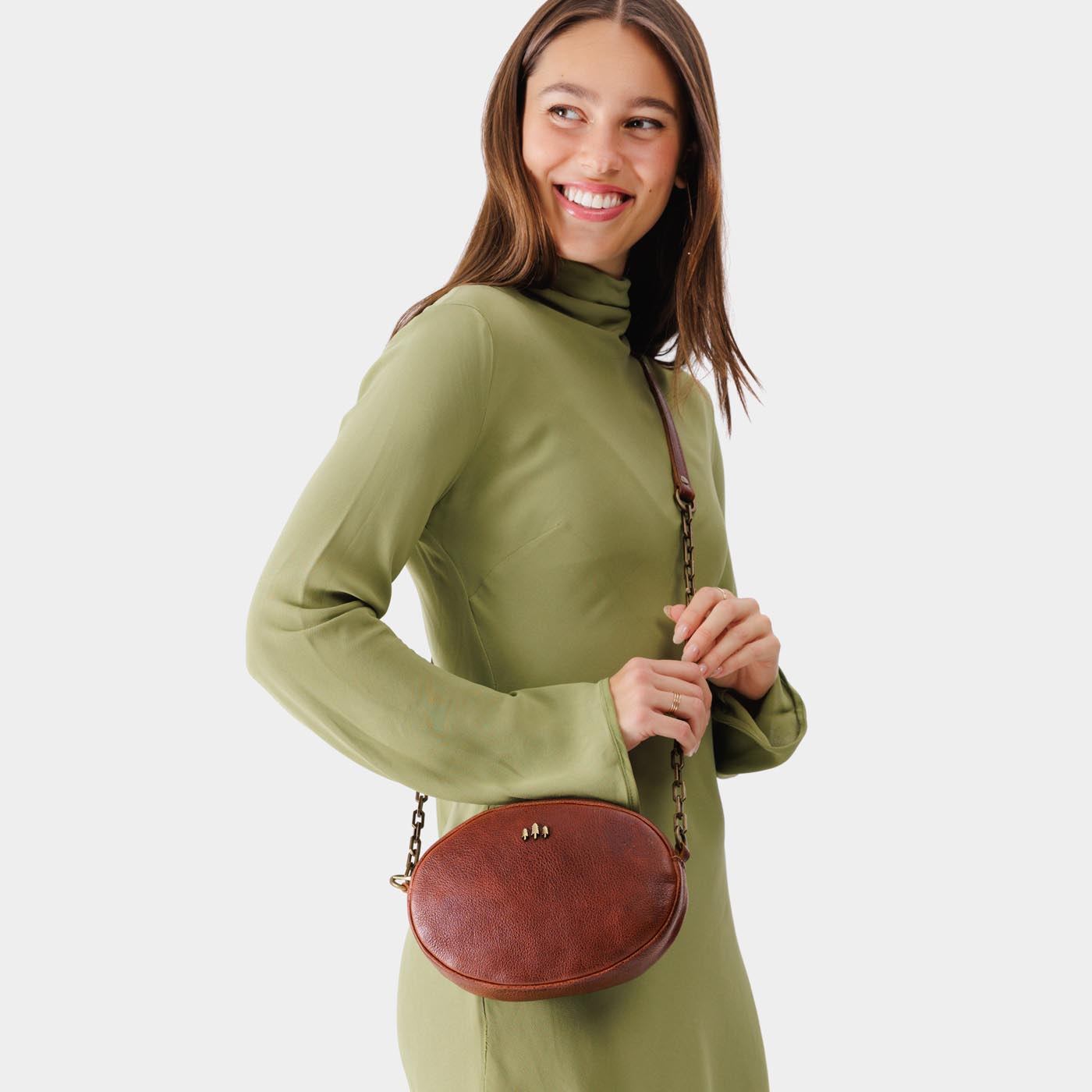 Nutmeg | Model wearing oval leather purse with metal crossbody chain strap and adjustable leather shoulder guard