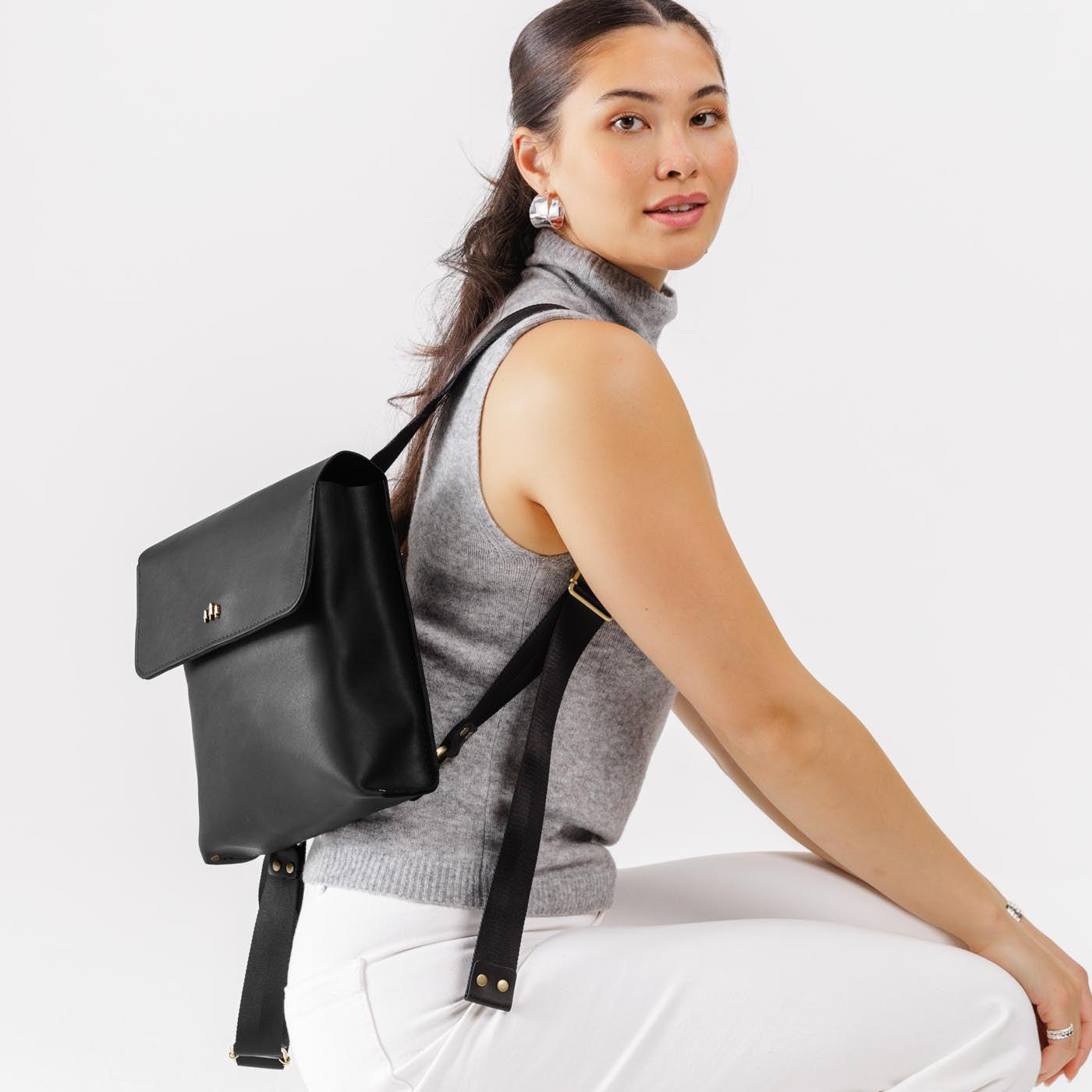 Black | Model wearing rectangular backpack with leather lined nylon straps and magnetic flap closure