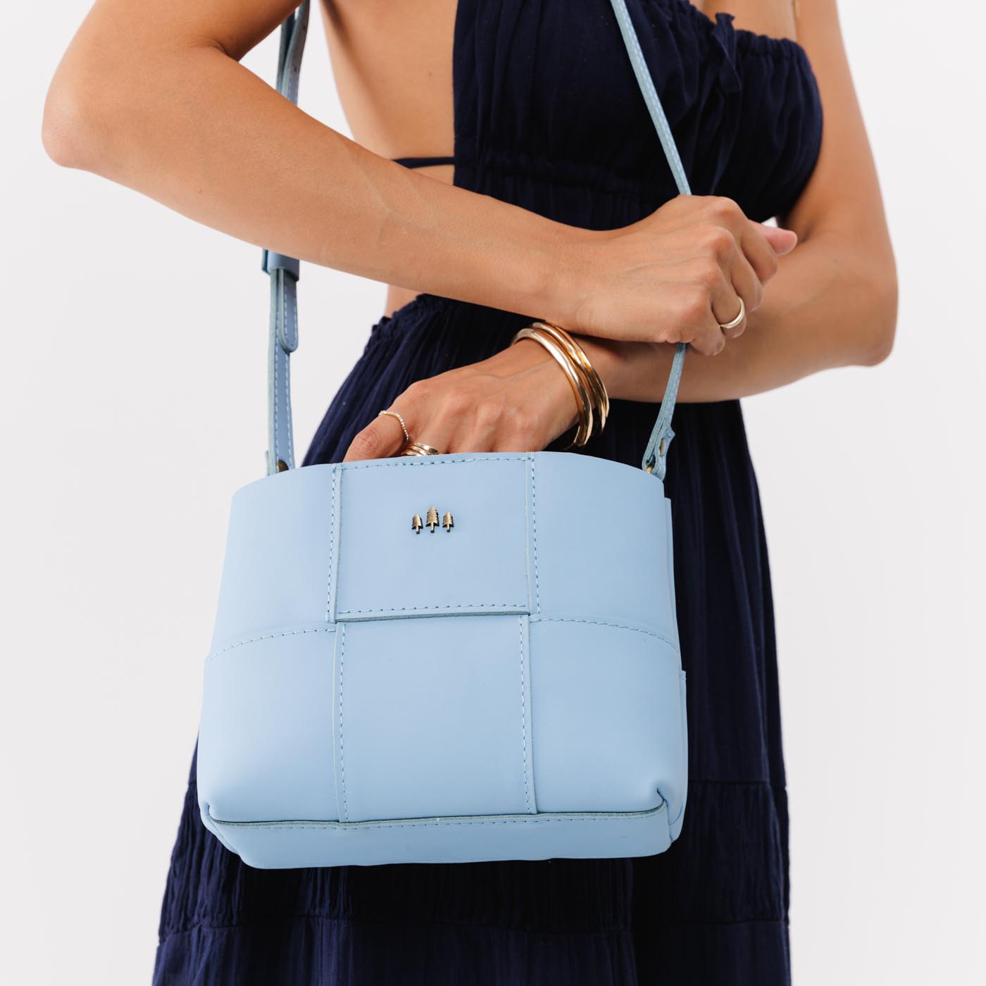 Glacial Blue*Small | Model carrying structured woven leather bag with three metal tree emblems and crossbody strap