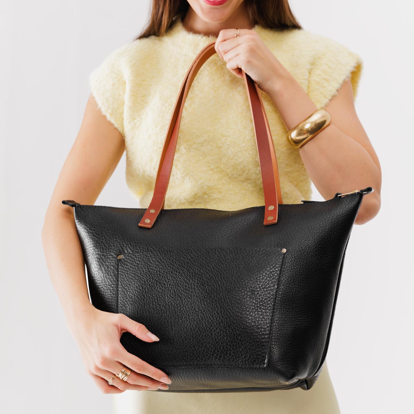 Pebbled--black Zipper | Model holding large leather tote bag with sturdy bridle handles and front pocket